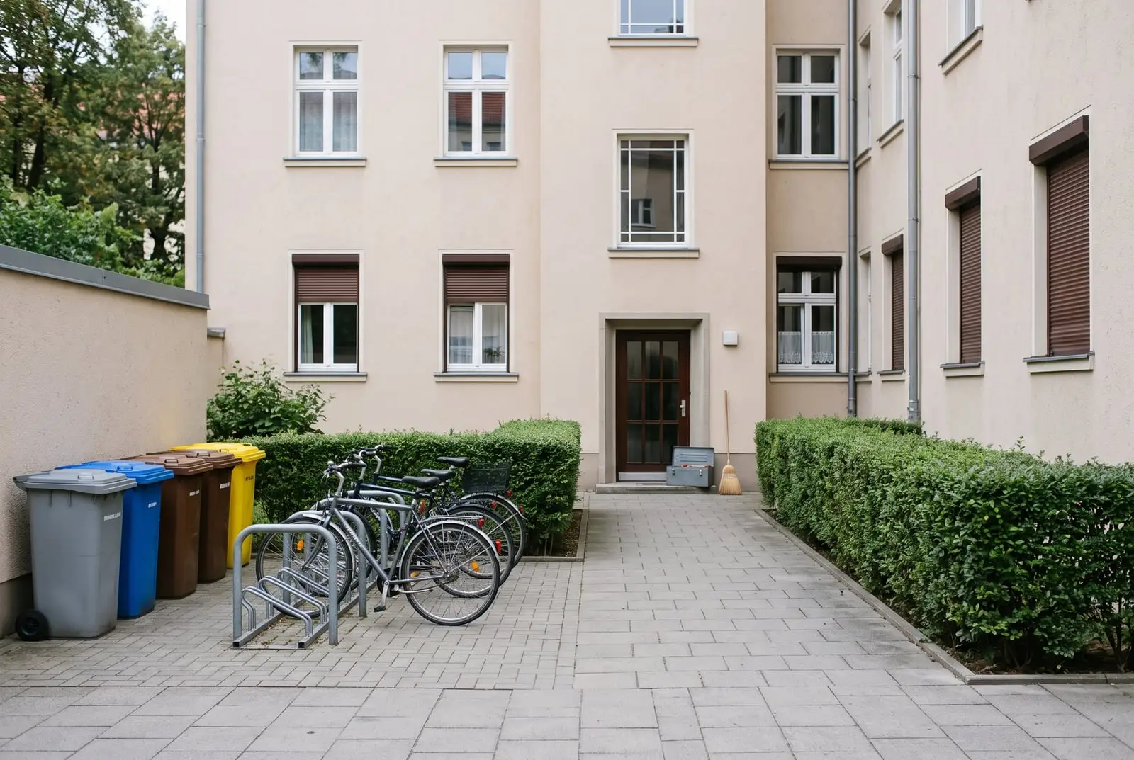 Gepflegter Innenhof einer Wohnanlage mit Mülltonnen und Werkzeug (Symbolbild)
